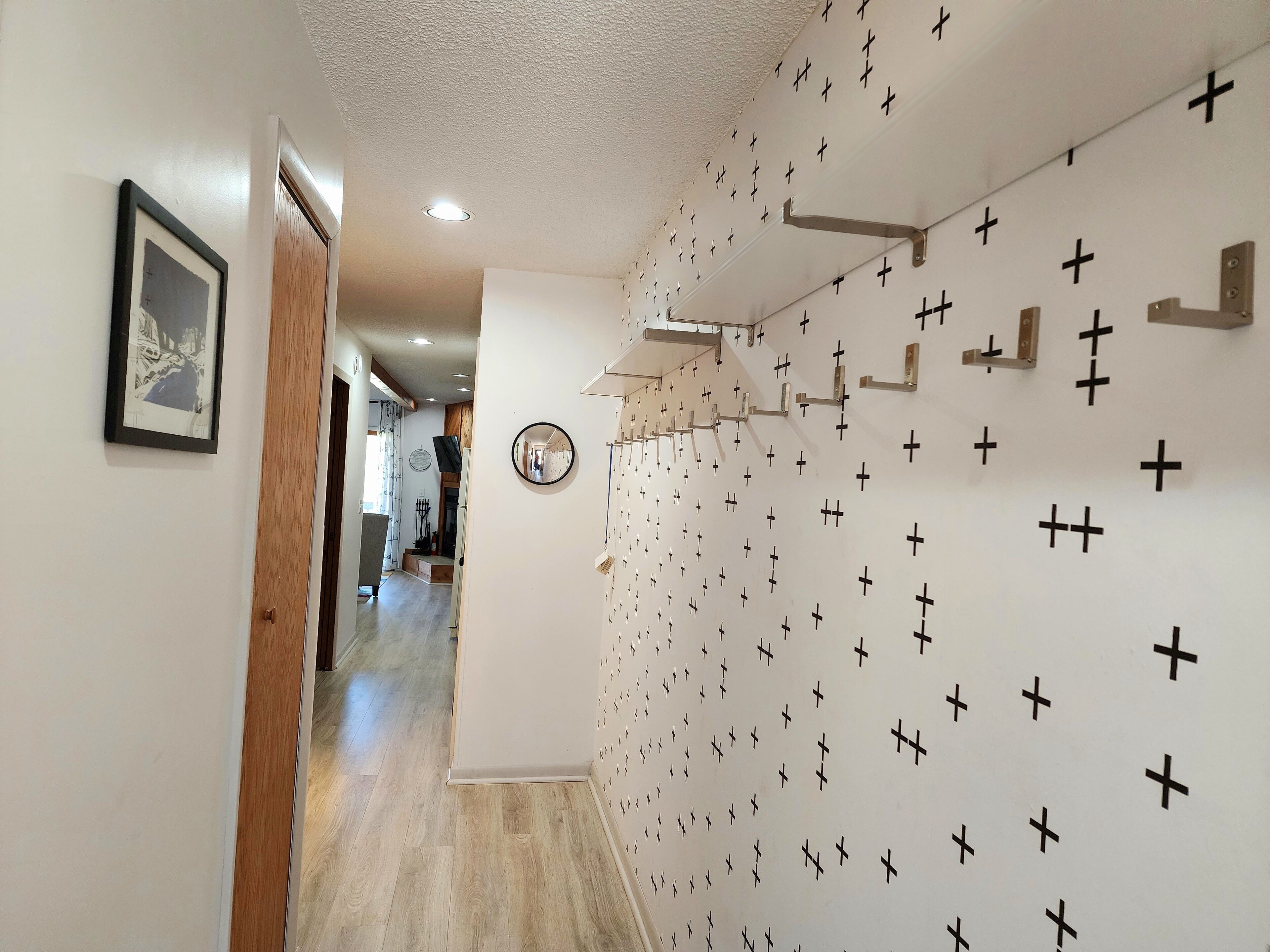 A hallway with a wall decorated with black crosses, a framed picture, and a round mirror.