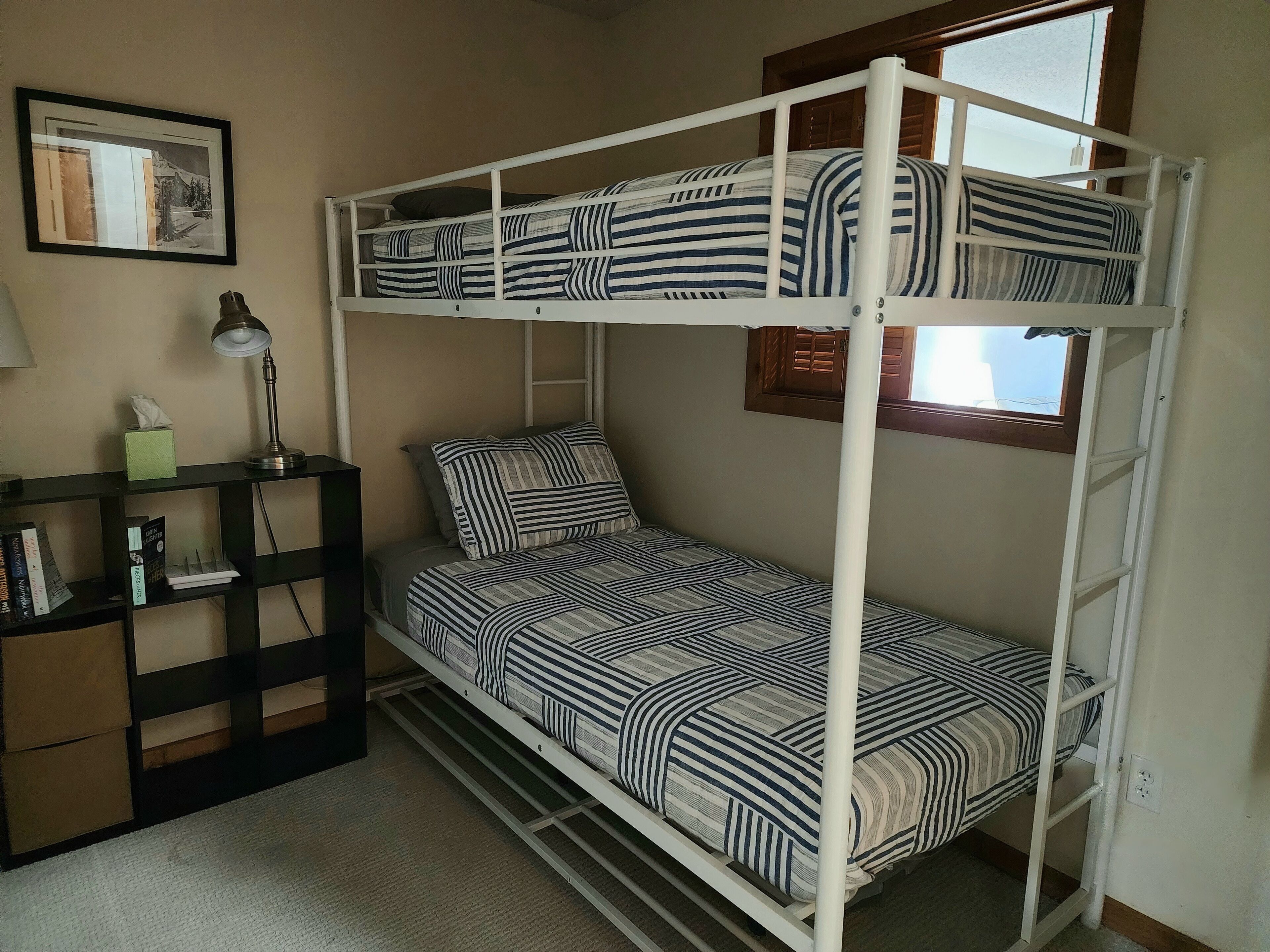 A bunk bed room with striped bedding, a desk with a lamp, and a bookshelf.