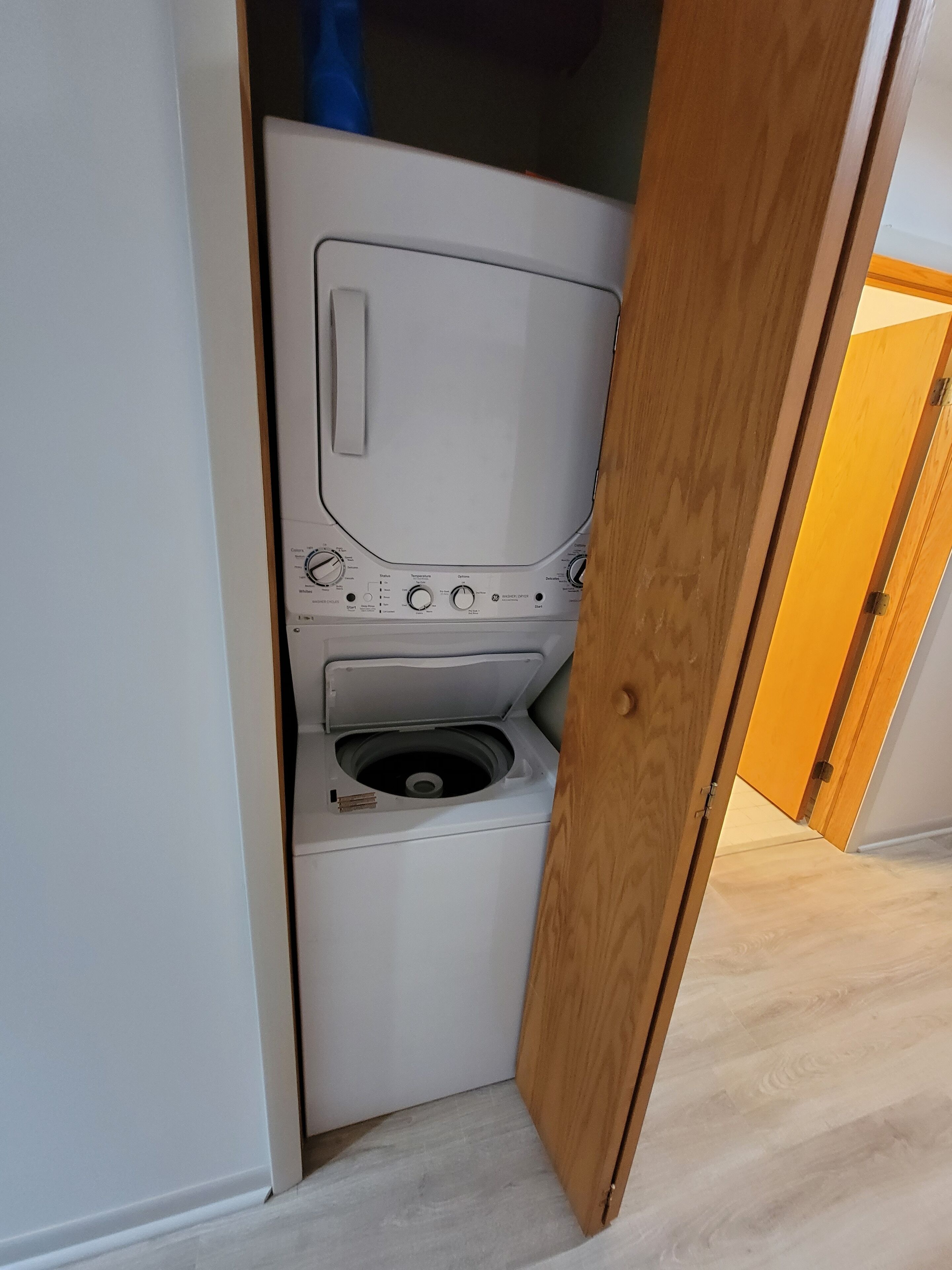A compact, white laundry room with a built-in washer and dryer, a small sink, and a wooden door leading to another room.