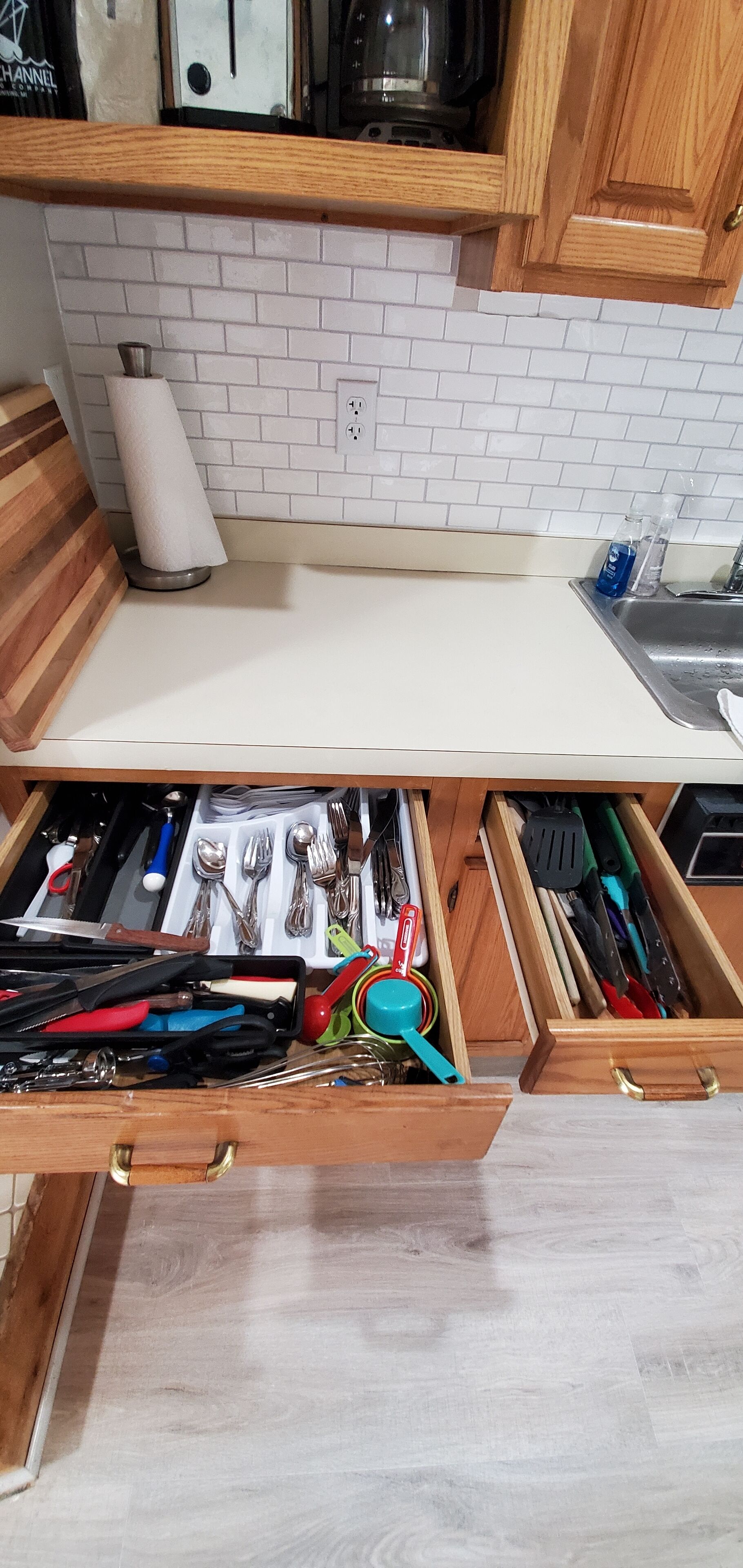 Une cuisine avec un dosseret de carrelage blanc, des armoires en bois et un plan de travail muni d’un porte-essuie-tout et d’un distributeur de savon.