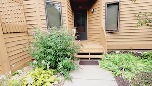A wooden house with a front porch, a small garden, and a mailbox. - 2 bedroom 2 full baths, Outdoor heated pool, sleeps 6, Near LAKES, Schuss course (Mancelona)