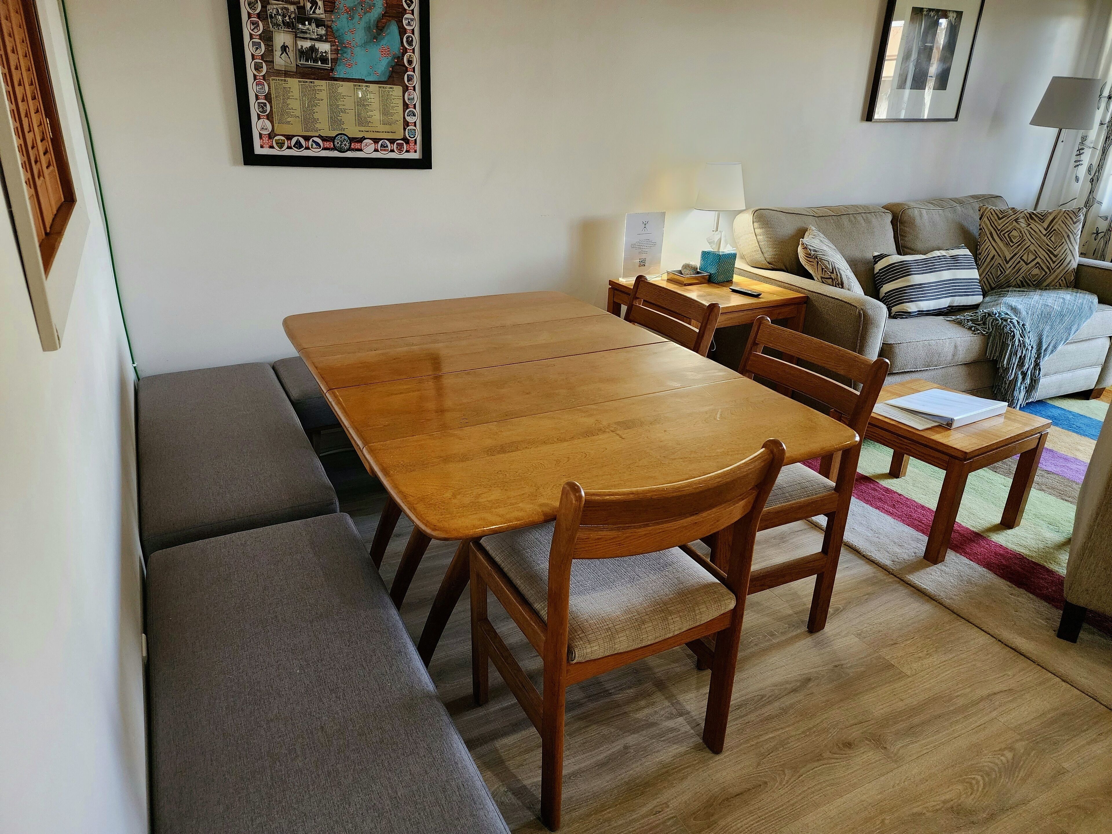 Uma sala de jantar com mesa e bancos de madeira, um sofá e uma luminária.