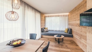 Una habitación moderna con una pared de madera, un sofá con cojines, una mesa de comedor con un cuenco de fruta y lámparas colgantes.