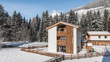 A modern building with a wooden facade, surrounded by snow-covered trees and a clear sky.