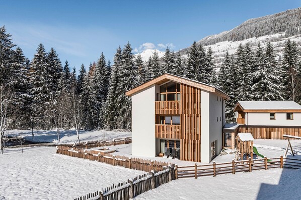 A modern building with a wooden facade, surrounded by snow-covered trees and a clear sky.