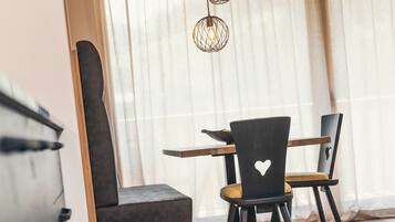 Een eethoek met een tafel en stoelen, een raam met dunne gordijnen, en een hanglamp.