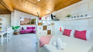 Un interior moderno con techo de madera, una cama con ropa de cama rosa y blanca, un sofá rosa, un escritorio blanco y una estantería con un cartel que dice 'RELAX'.