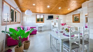 Un interior moderno con techo de madera, un sofá rosa, una mesa de comedor con sillas blancas y un televisor en la pared.