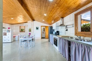 A kitchen with wooden ceiling, white walls, and a large window.