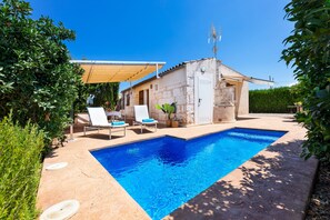 A swimming pool with lounge chairs, a small building, and a clear blue sky.