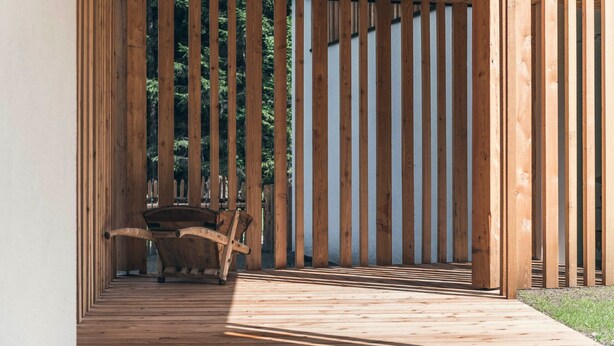 Une terrasse en bois avec un banc et une table, entourée de lattes de bois verticales.