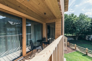 A wooden deck with a glass door leading to a room, a small table with chairs, and a wooden railing.