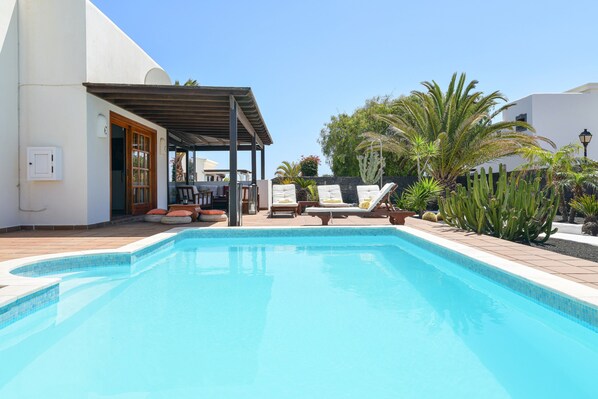 A swimming pool with lounge chairs and a covered seating area.
