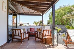 A covered patio area with wooden furniture, a glass door leading outside, and a stone wall in the background.