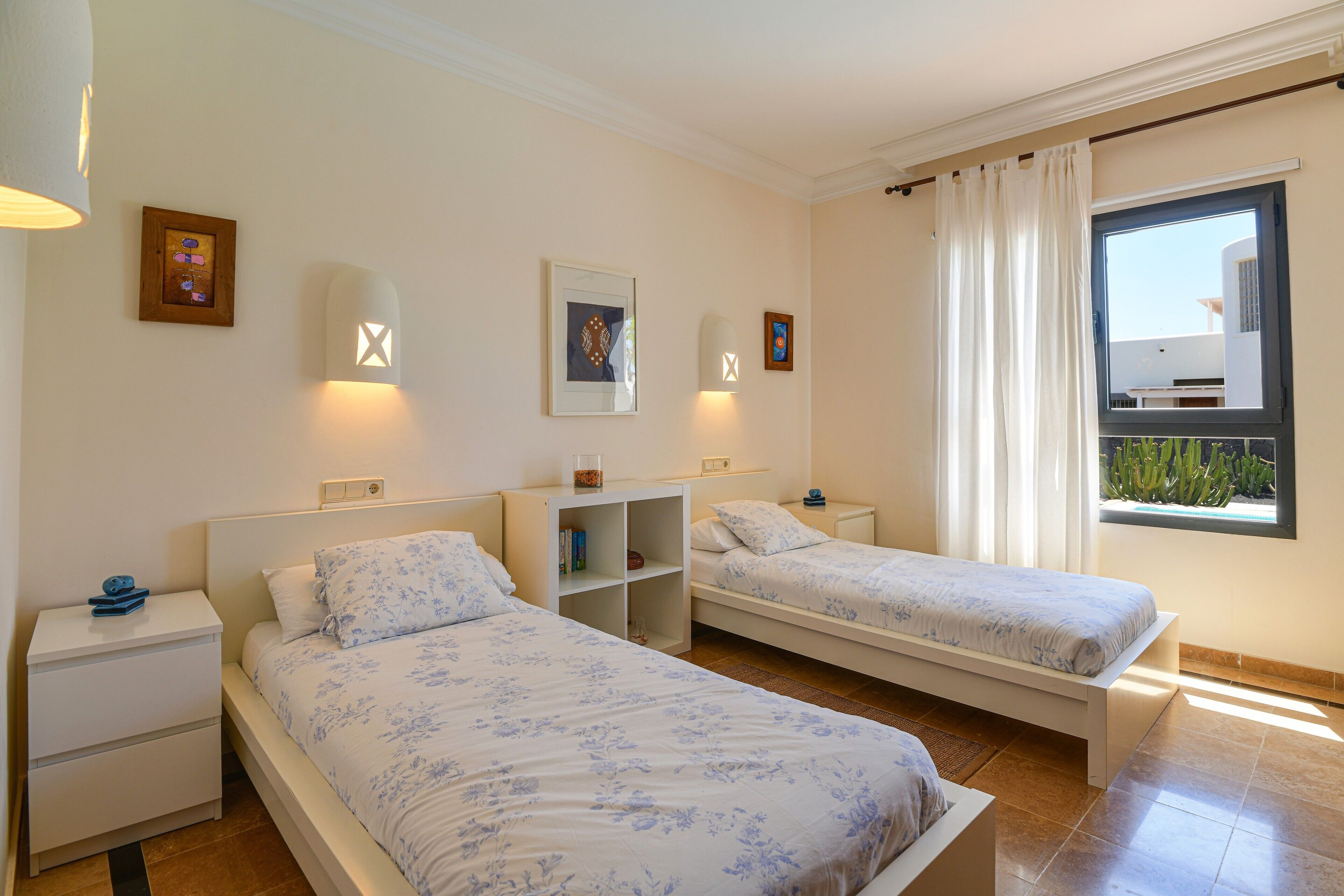 A bedroom with two beds, a nightstand, a shelf, and a window with curtains.
