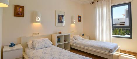 A bedroom with two beds, a nightstand, a shelf, and a window with curtains.