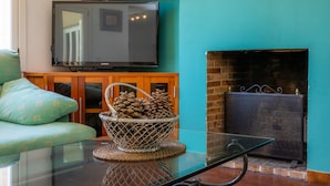 A living room with a television, a fireplace, a sofa, and a table with a basket of pinecones.