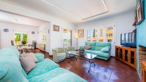 A living room with a sofa, chairs, a glass coffee table, and a television.