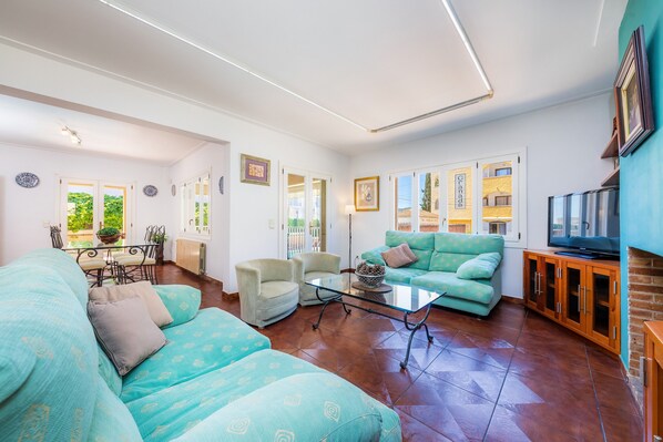A living room with a sofa, chairs, a glass coffee table, and a television. - Villa "Paca" with Pool, Air Conditioning, Fireplace, Wi-Fi & Garden (Cala Ratjada)