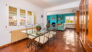 A dining area with a glass table and chairs, a kitchen with teal walls, and a view through the window.