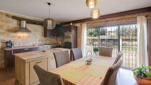 A kitchen with a central island, dark cabinetry, and a dining area with wicker chairs and a striped tablecloth.