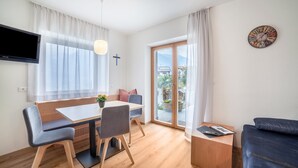 Ein modernes Zimmer mit Esstisch, Stühlen, einer Couch, einem Fernseher und einem großen Fenster mit Vorhängen.