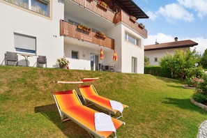 A building with a balcony, outdoor seating, and a grassy slope.