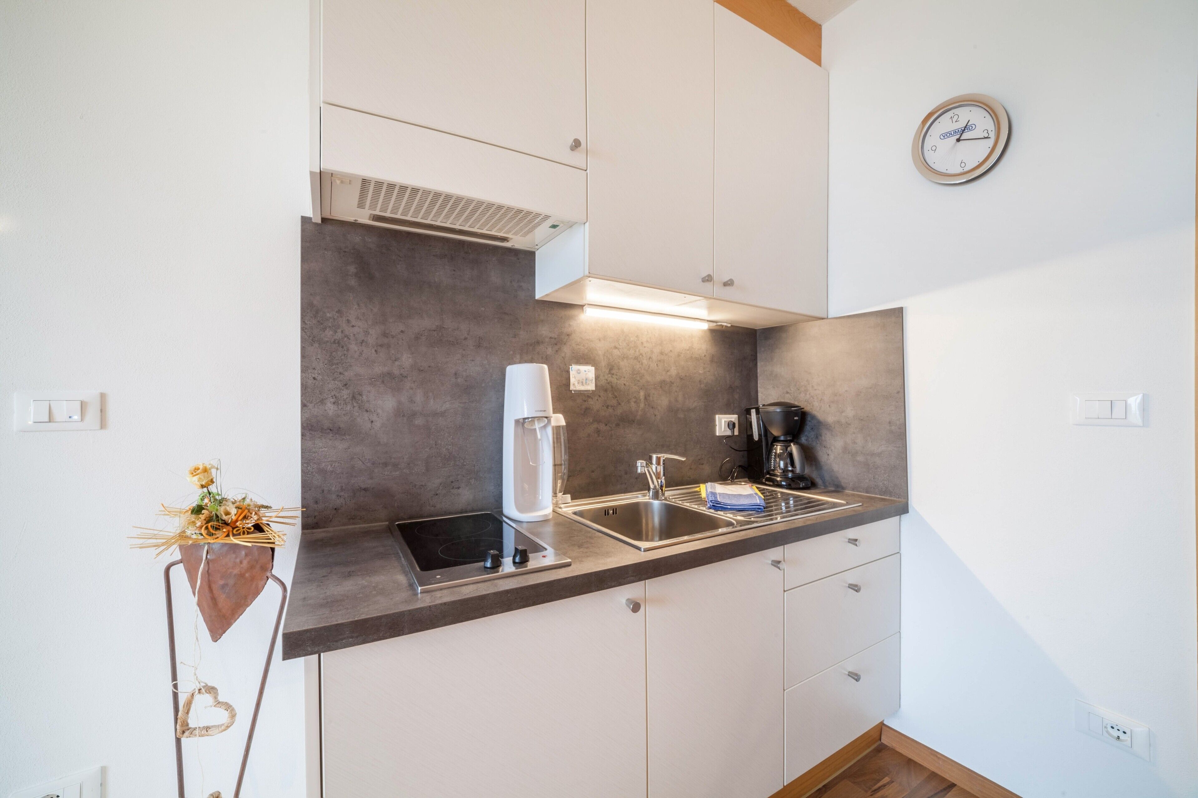 Une cuisine moderne avec des armoires blanches, une cuisinière encastrée, une machine à café et une horloge murale.