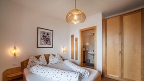 A bedroom with a wooden bed, a bedside table, a wall-mounted light, a framed picture, and a wardrobe. - Apartment "Haus Hohenrain 3" with Mountain View, Pool, Wi-Fi, Terrace & Garden (Schenna)