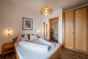 A bedroom with a wooden bed, a bedside table, a wall-mounted light, a framed picture, and a wardrobe.