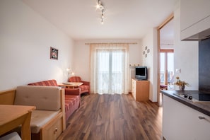 A compact living space with a sofa, a small table, a TV, and a kitchenette.
