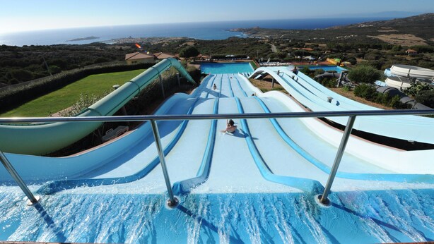 Un parc aquatique doté de nombreux toboggans et d’une piscine, entouré d’un paysage vallonné et avec la mer en toile de fond.
