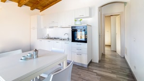 Une cuisine moderne avec des meubles blancs, un four encastré et un coin repas comprenant une table et des chaises.