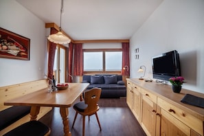 Une pièce chaleureuse avec une table à manger en bois, un canapé, un téléviseur et une fenêtre avec des rideaux.