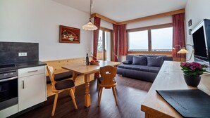 A modern kitchen with wooden cabinets, a dining table with chairs, a sofa, and a TV. - Apartment "Haus Hohenrain 4" with Mountain View, Pool, Wi-Fi, Balcony & Garden (Schenna)