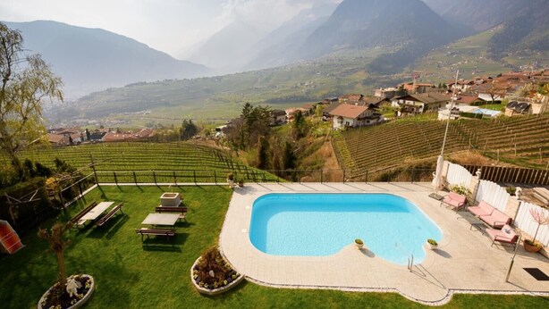 A swimming pool with a view of a mountainous landscape and a village. - Apartment "Haus Hohenrain 4" with Mountain View, Pool, Wi-Fi, Balcony & Garden (Schenna)