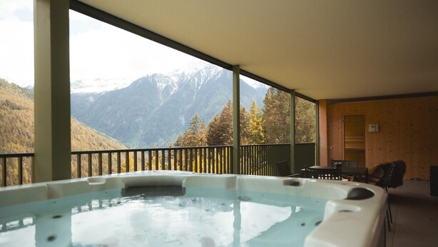 Un bain à remous avec vue sur les montagnes, des murs en bois et un balcon avec des chaises.
