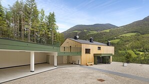 A modern building with a wooden facade, a covered outdoor area, and a view of a mountainous landscape.
