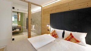 A bedroom with a bed, a wooden headboard, a glass shower enclosure, and a bathroom with a sink and mirror.
