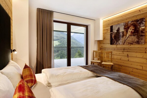 A hotel room with two beds, a large window with a view of a balcony, and a wooden wall with a framed picture.