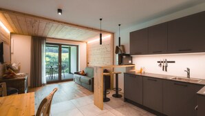 A modern kitchen with wooden cabinets, a dining area with a wooden table and chairs, and a cozy seating area with a sofa and a view of the outdoors.