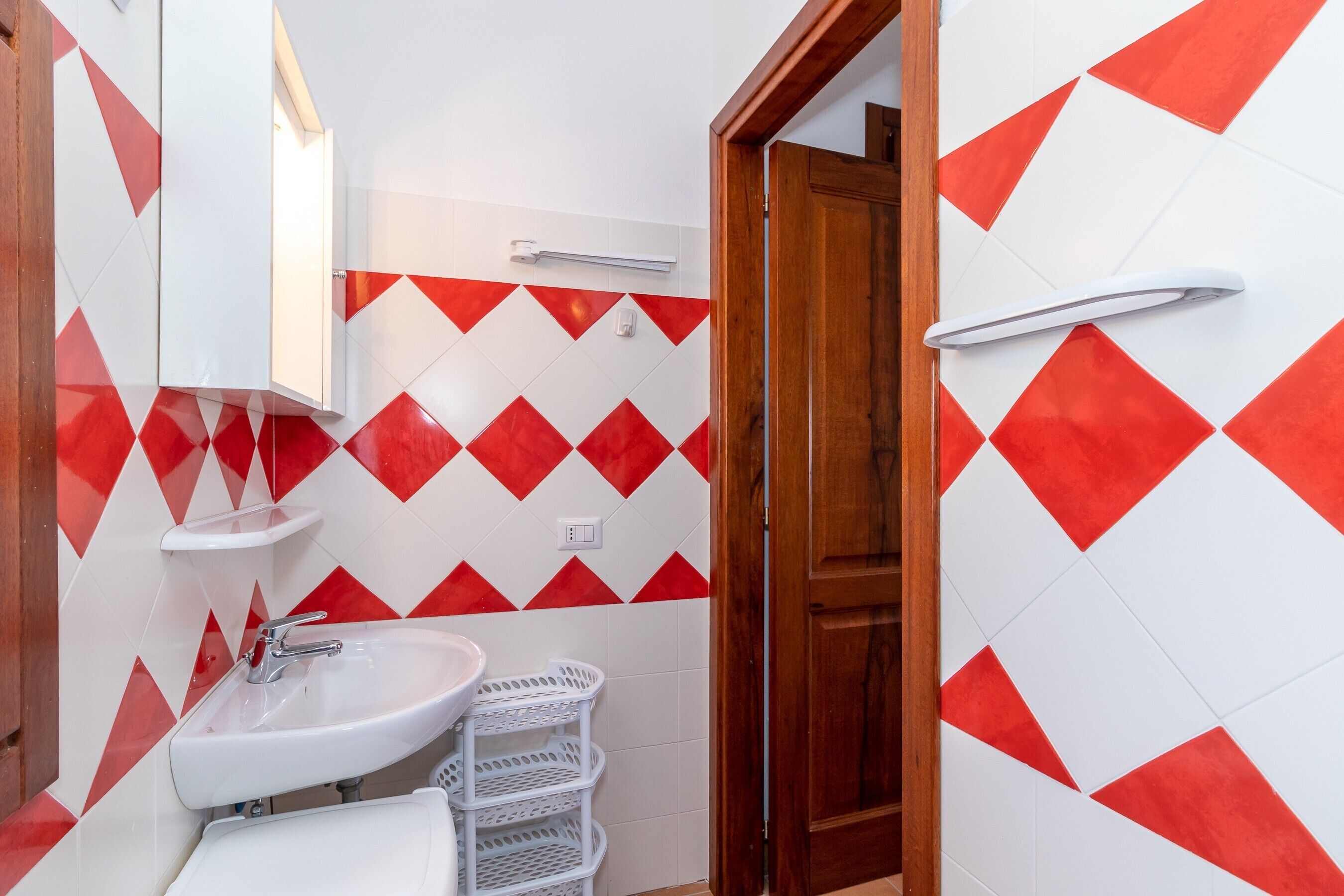 Un baño con un lavamanos blanco, un espejo y una pared con diseño a rombos en blanco y rojo.