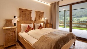 Un dormitorio con cama de madera, dos mesitas de noche, un ventanal con vistas a un paisaje verde y un cerramiento de vidrio corredizo hacia un balcón exterior.