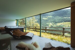 Una habitación moderna con un ventanal grande, un jacuzzi y una terraza de madera con vistas a un valle boscoso.