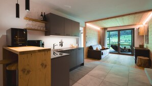 Una cocina moderna con una isla central, estanterías de madera y un comedor con sofá y vistas al exterior.