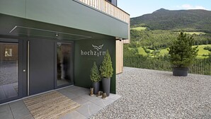 A modern building with a green facade, a wooden balcony, and a view of a mountainous landscape. - Apartment "Archehof Hochzirm Lodge Franz" with Mountain View, Sauna & Terrace (Campo Tures)