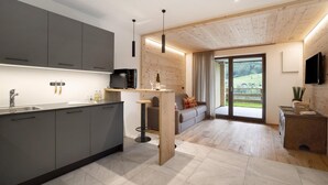 A modern kitchen with grey cabinets, a black microwave, and a wooden dining area with a sofa and a table. - Apartment "Archehof Hochzirm Lodge Franz" with Mountain View, Sauna & Terrace (Campo Tures)