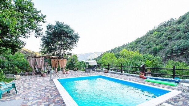 Una piscina rettangolare con bordo piastrellato, circondata da vegetazione e un paesaggio collinare.