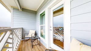 Un balcon doté d’un plancher en bois, d’une chaise avec des coussins et d’une porte vitrée donnant sur une vue panoramique de la ville.