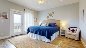Une chambre à coucher comprenant un lit, une table de chevet, une chaise, un ventilateur de plafond et une porte donnant sur un balcon.